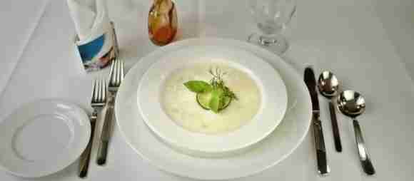 Bowl of Avgolemono soup garnished with fresh herbs on a white table setting.