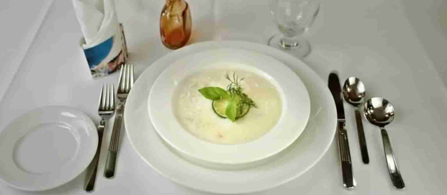 Bowl of Avgolemono soup garnished with fresh herbs on a white table setting.