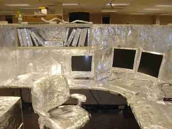 Office workspace with foil-covered cubicle, computer monitors, and ergonomic chair.