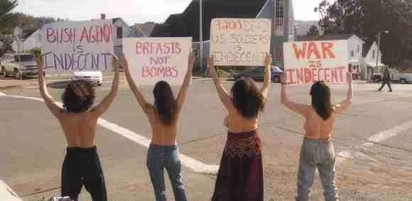 Alt text: Group of women protesting topless, holding signs about anti-war and anti-war messages.