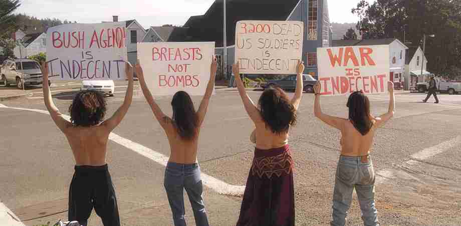 Alt text: Group of women protesting topless, holding signs about anti-war and anti-war messages.