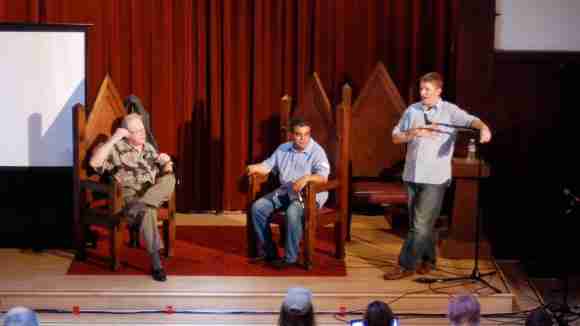 Three men engaged in a discussion on a stage during a panel event.
