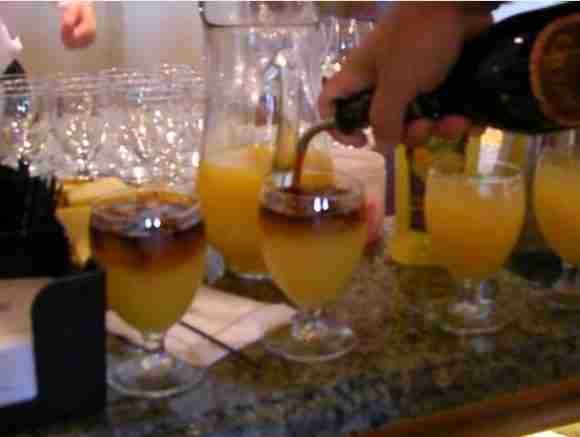 Pouring champagne into glasses of orange juice at a party.