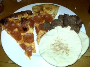 Pizza slice with pepperoni, beef, and flatbread on a white plate.