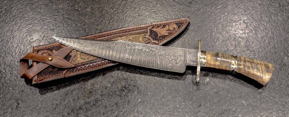 Damascus steel knife with ornate handle and leather sheath, showcasing traditional bladesmithing cra.