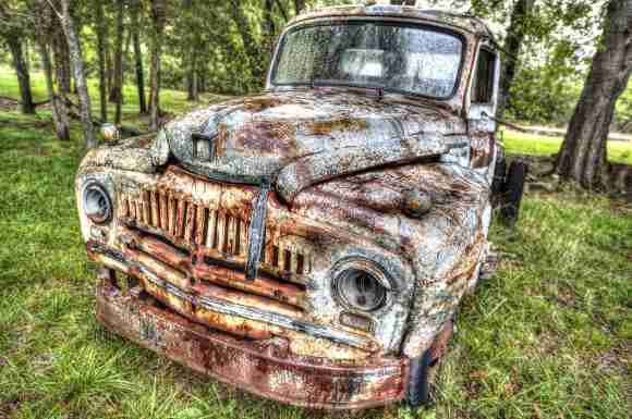 Rusty vintage truck in a forest clearing with green trees and grass.