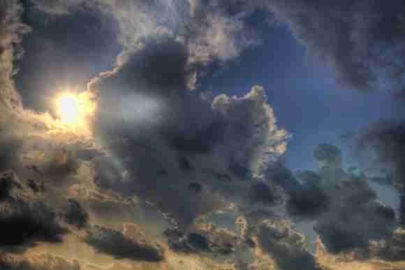 Sun shining through dark, dramatic clouds in a partly cloudy sky.