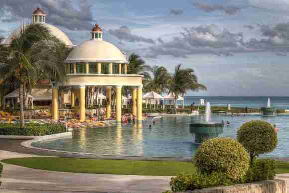 Luxury resort pool with domed pavilion, palm trees, and ocean view, perfect for relaxation.