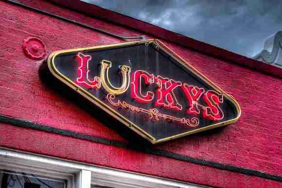 Neon sign reading "Lucky's" on a red brick building exterior.