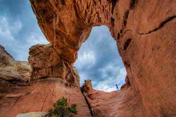Red rock arch formation in a canyon with a bright blue sky overhead.