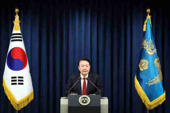 South Korean official speaking at a press conference with flags in the background.